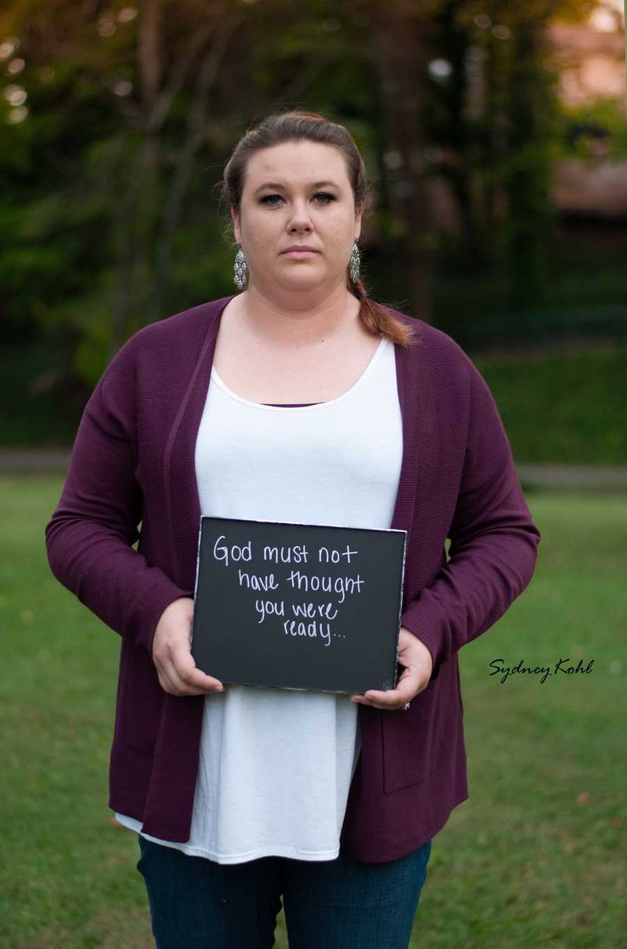 Woman who experienced child loss holds sign that says, "God must have not thought you were ready"