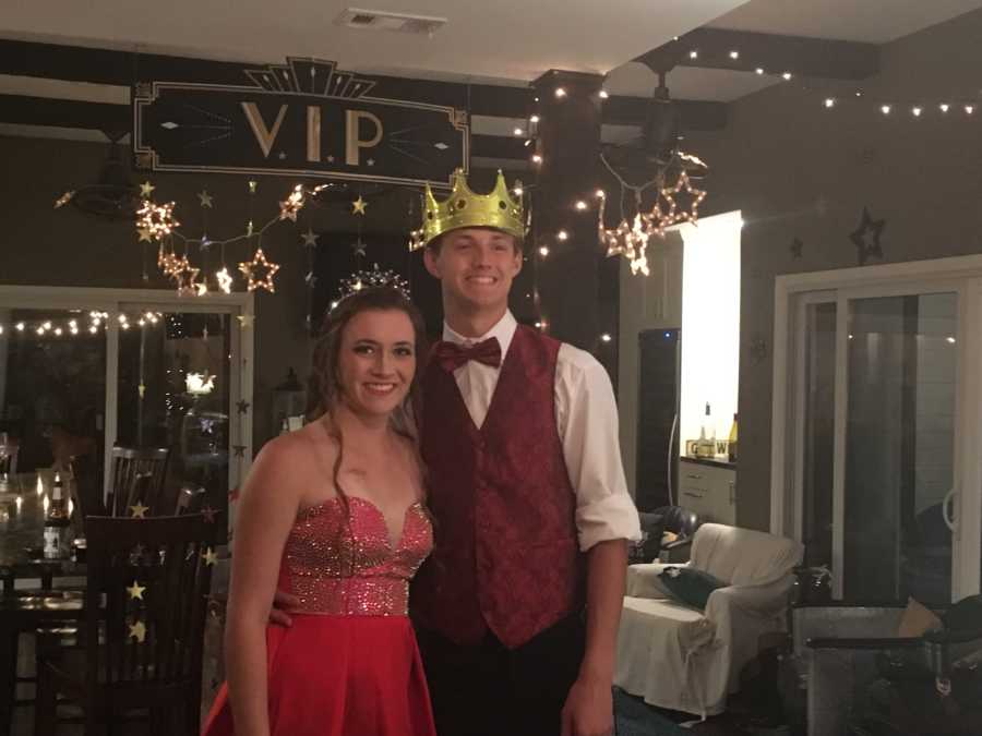 Teen couple who missed prom stand smiling in living room that was turned into prom scene