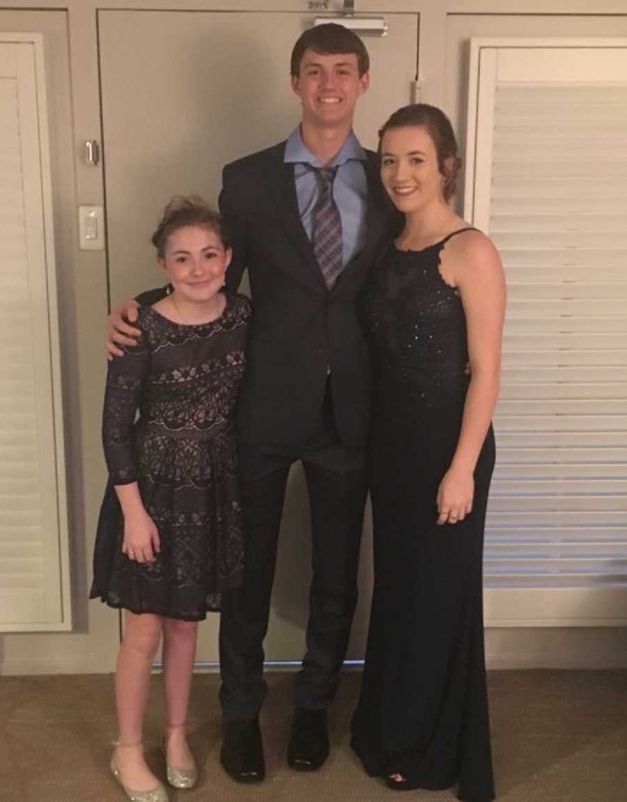 Teen stands smiling with arms around girlfriend and little sister
