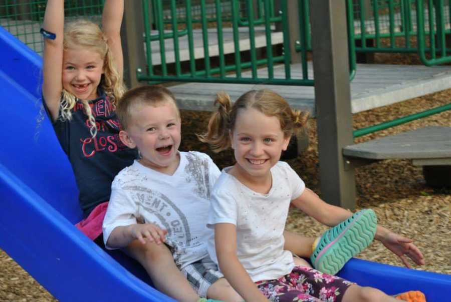 Two young girls and boy smile on slide whose parents are married to each other