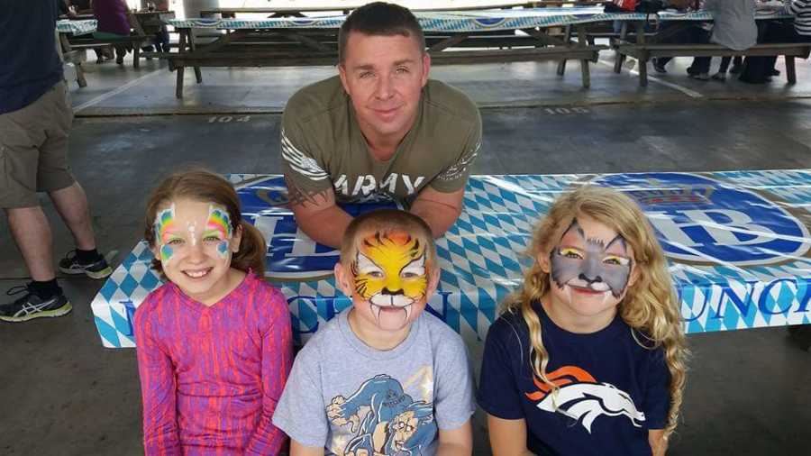 Man leans over table where his son and his wife's two daughters sit with face painting on