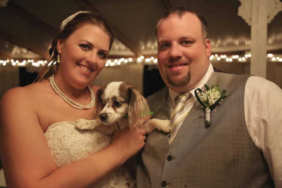 Bride and groom smile at wedding while bride holds their dog