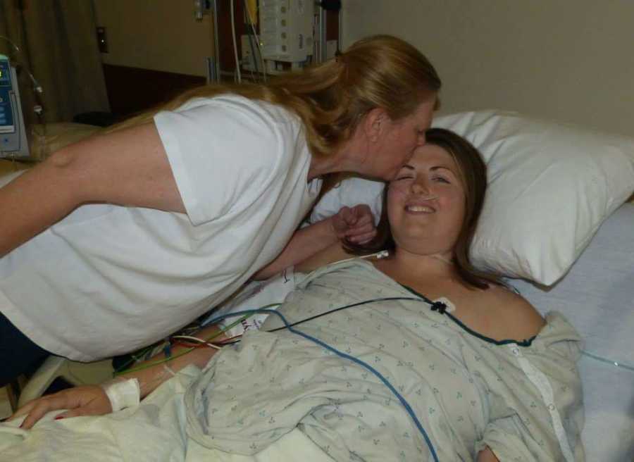Woman with Wegner’s Granulomatosis lies in hospital bed smiling as mother kisses her forehead