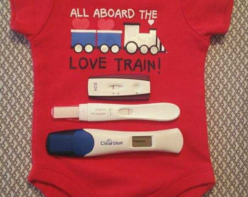 Onesie that says, "All aboard the Love Train" with three pregnancy tests on it