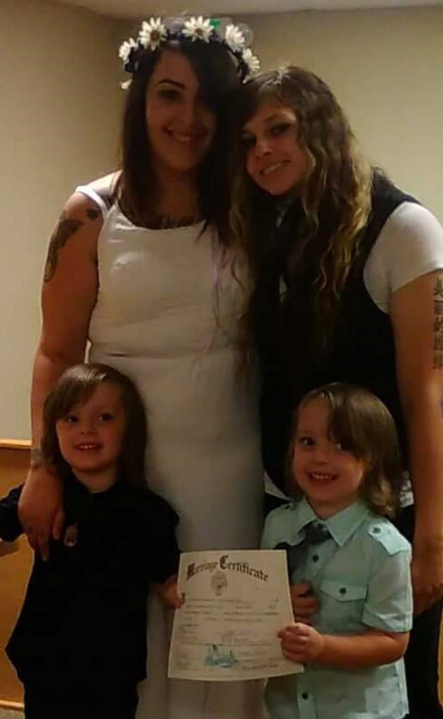 Brides stand smiling while on of the bride's son's holds marriage certificate