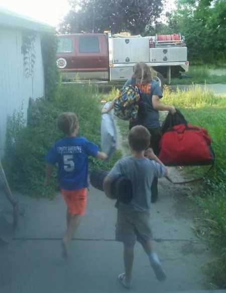 Mother walks on sidewalk with luggage while her twin boys follow