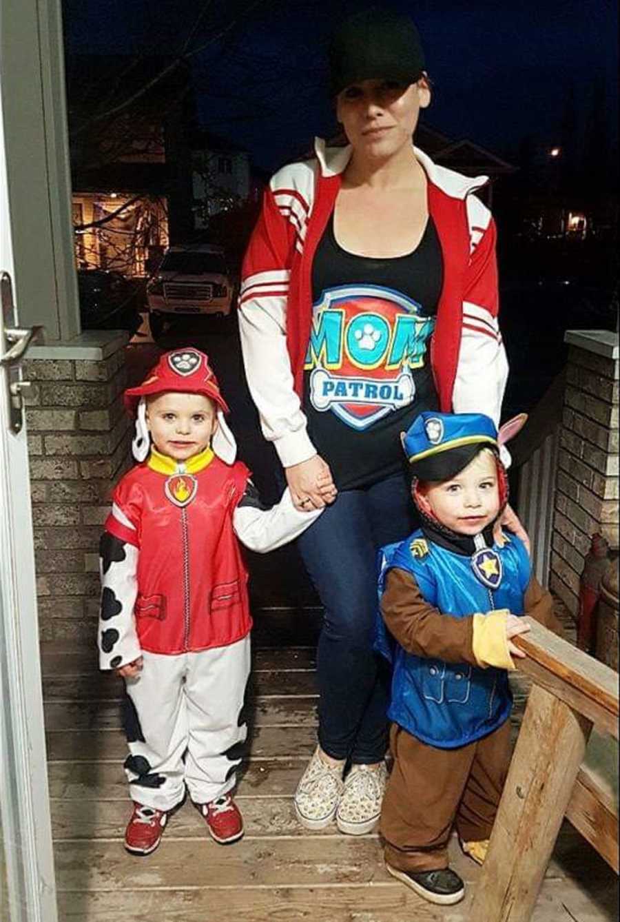 Mother stands with two kids on porch who are dressed in Paw Patrol costumes for Halloween