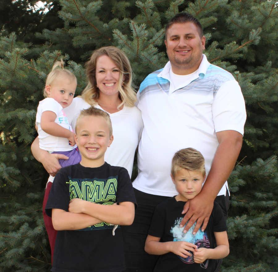 Woman who beat cancer stands holding daughter beside husband and two sons