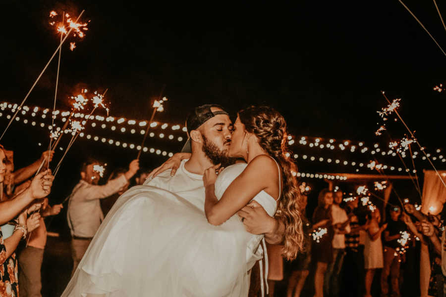Husband holds and kisses paralyzed bride while guests watch