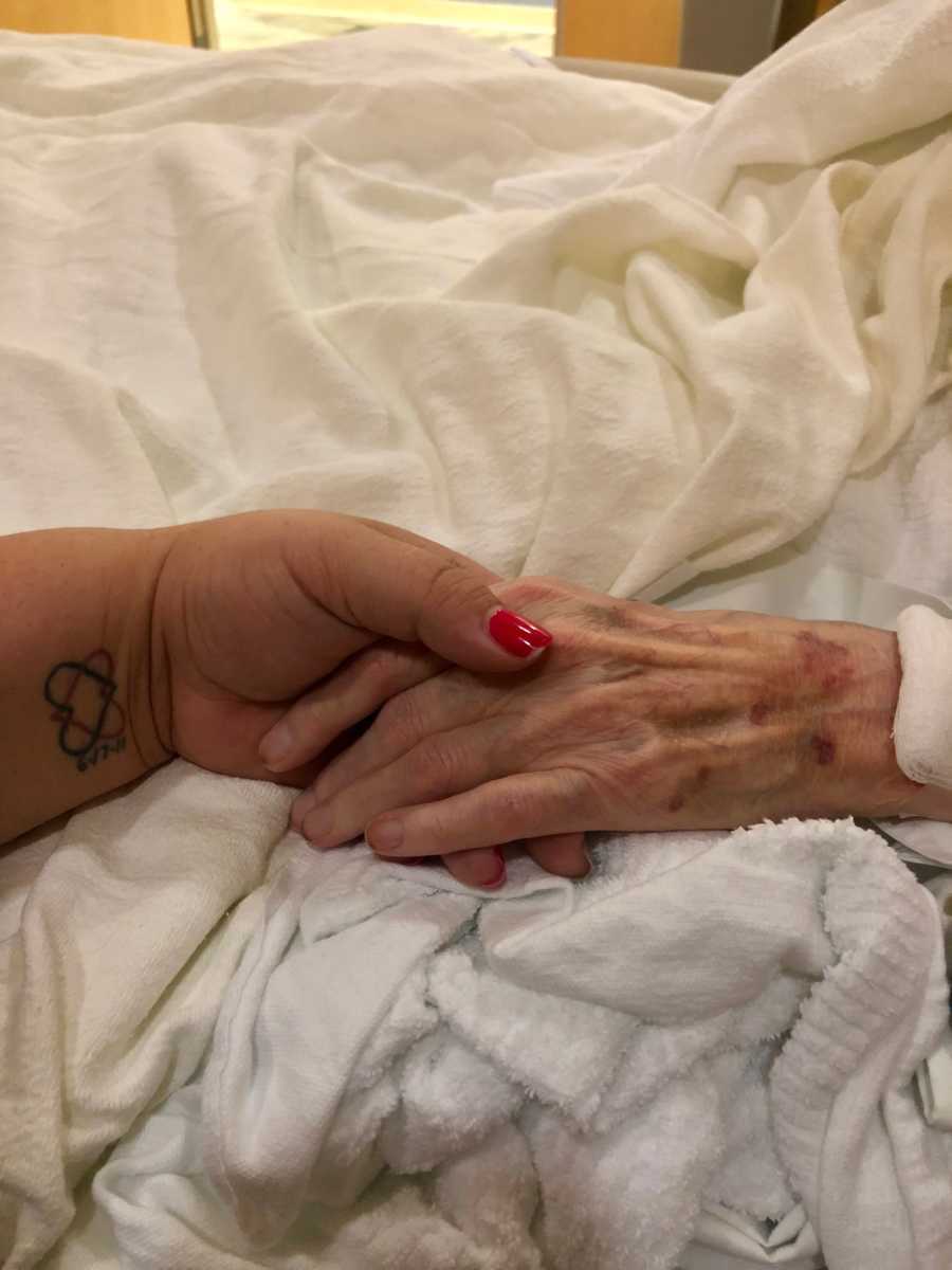 Close of up woman's hand holding grandmother's hand in hospital bed