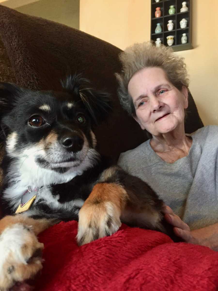 Elderly woman sits on couch smiling at dog sitting beside her on red blanket
