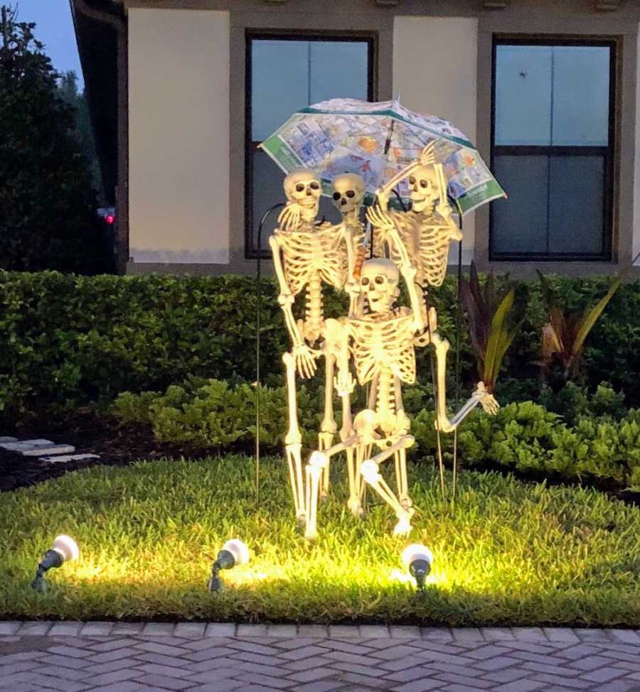 Five skeleton's stand in yard under umbrella