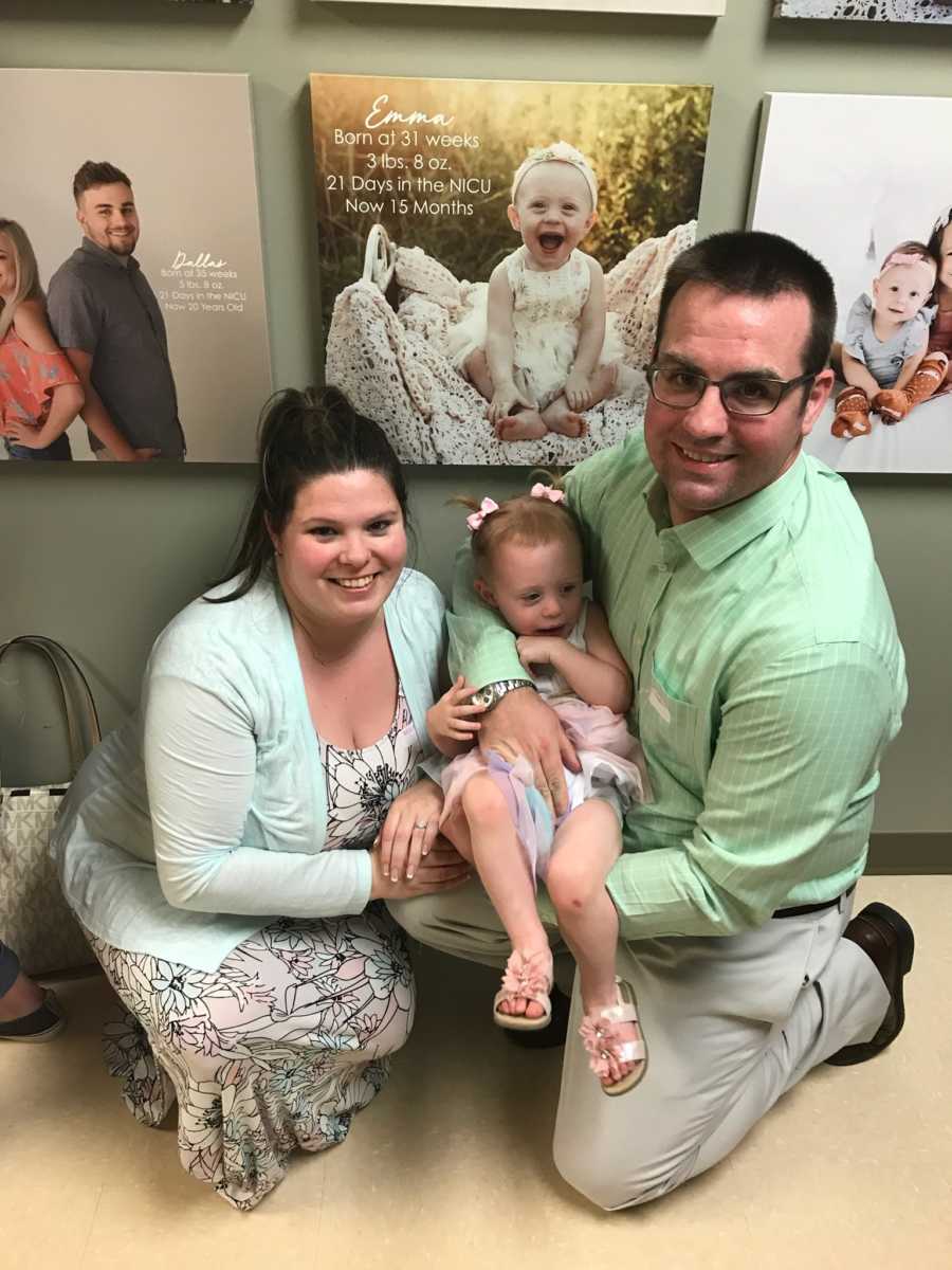 Mother and father hold daughter beside her image in hospital that says, "21 days in NICU"