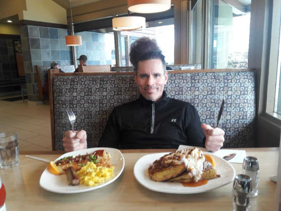 Man who had brain surgery to remove tumor sits in restaurant with two plates of food in front of him