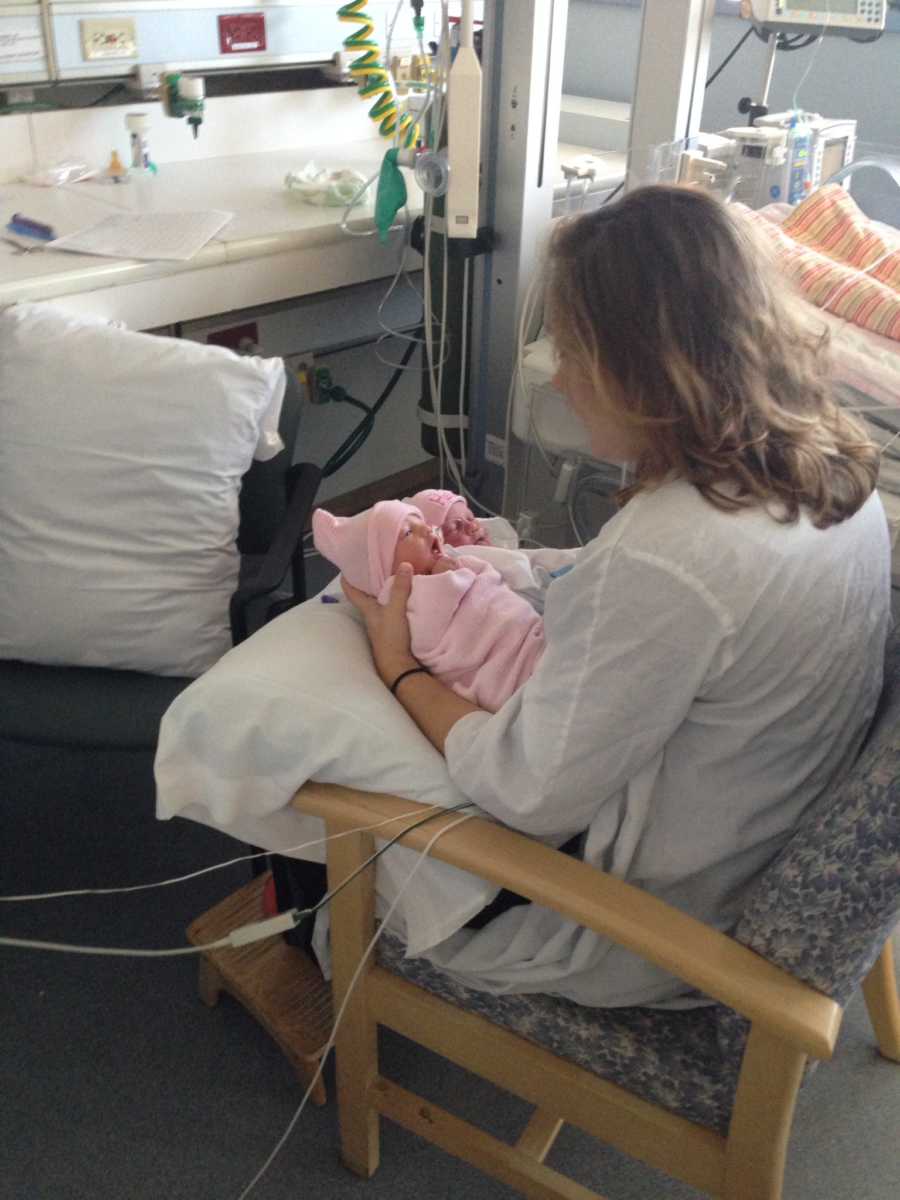 Mother sits in chair holding twin girls in NICU