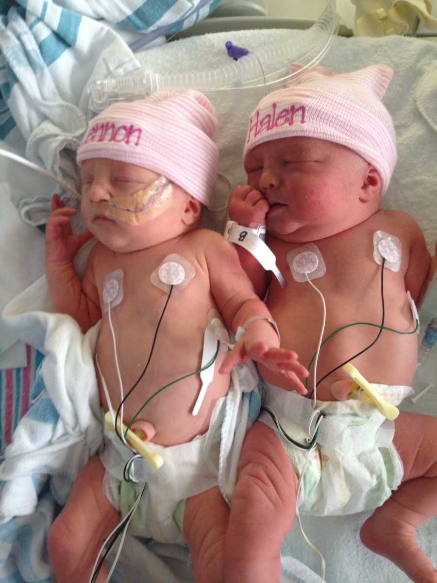 Newborn twin girls lay asleep in NICU with matching pink hats on