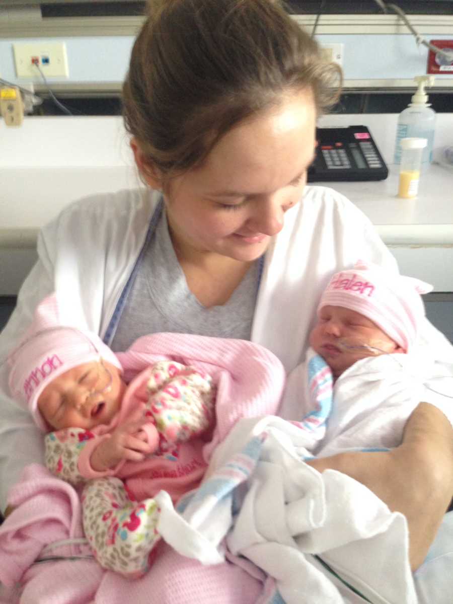 Mother smiles as she looks down at twin daughter's in her arms that have been in NICU