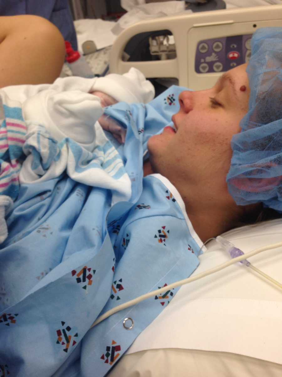 Woman who just gave birth lays in hospital bed holding newborn to her chest