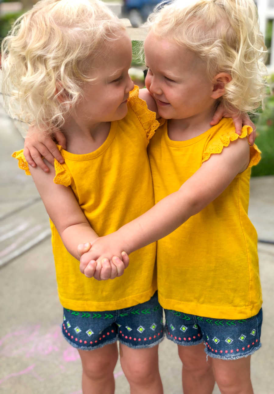 Twins girls in matching outfits hold hands while looking at each other