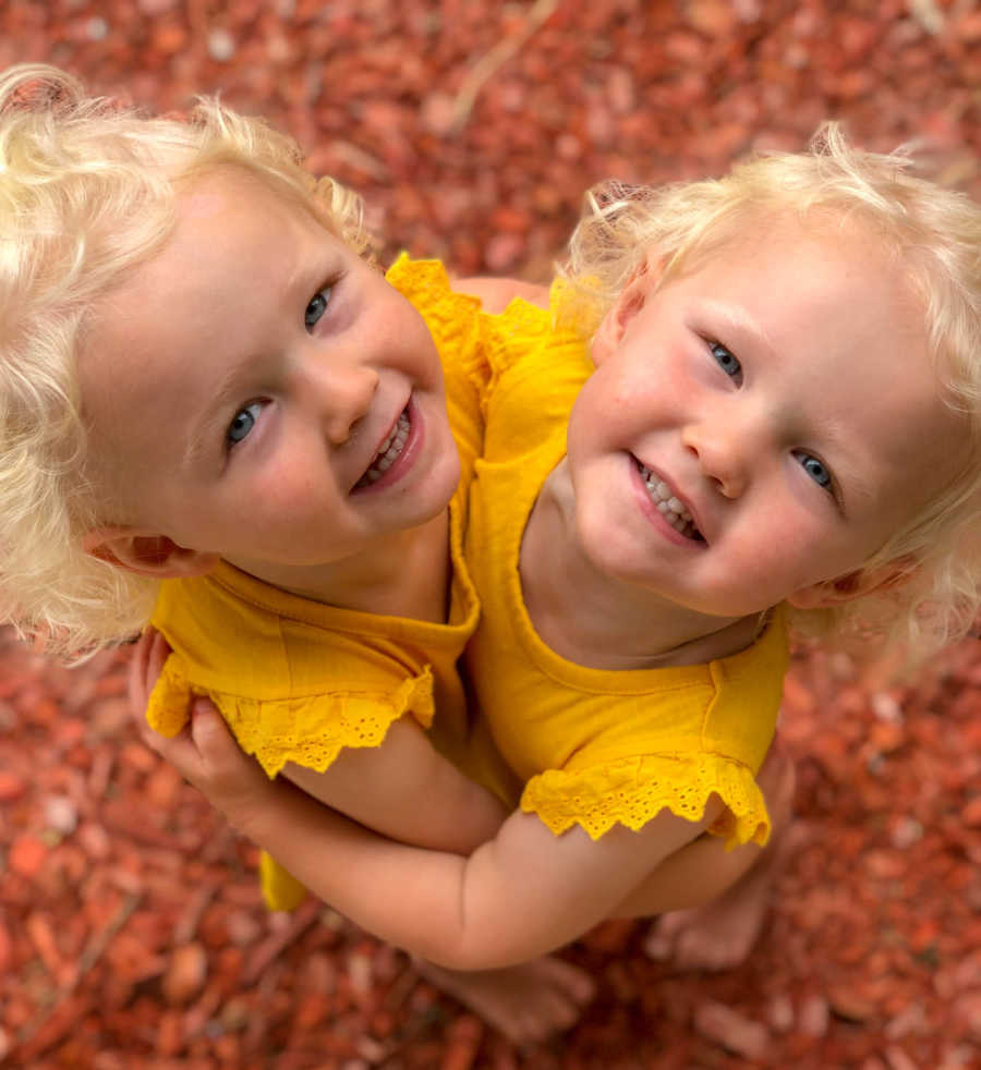 Twin girls hug in matching yellow dresses while looking up