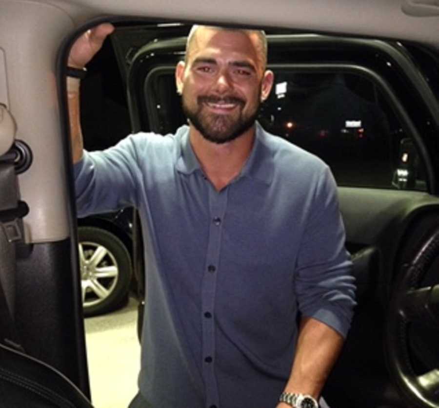 Man stands smiling beside car with open door