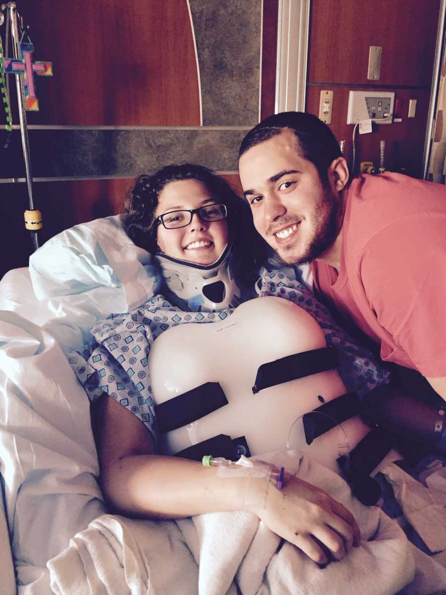 Woman sits in hospital bed with back and neck brace on smiling beside man