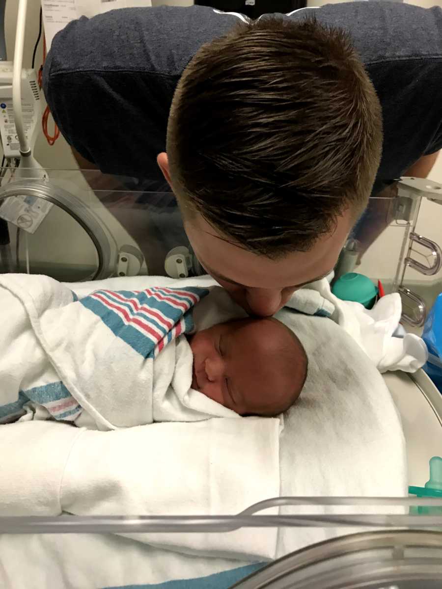 Father leans over and kisses newborn on head