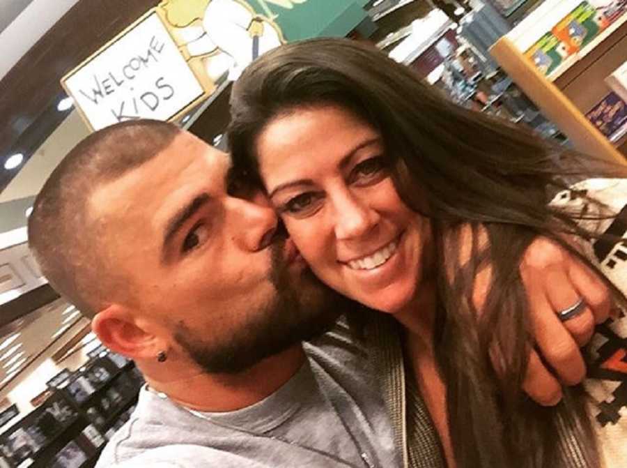 Husband kisses wife on cheek while she smiles for selfie