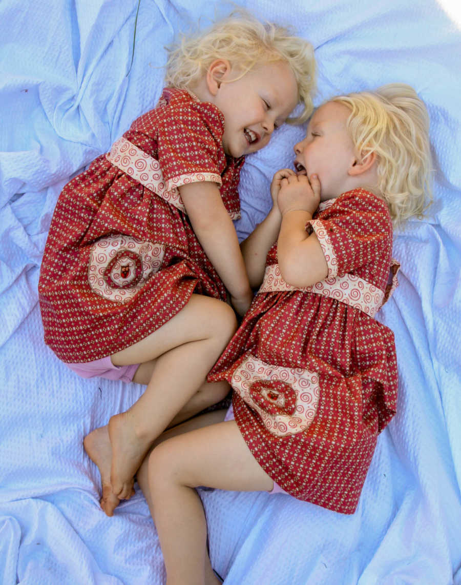 Twin girls lay on blue blanket in matching red dresses smiling