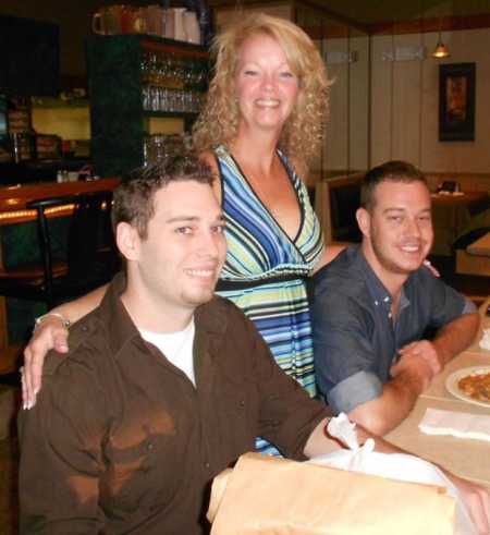 Mother standing in between two sons at restaurant table, one of which has passed away