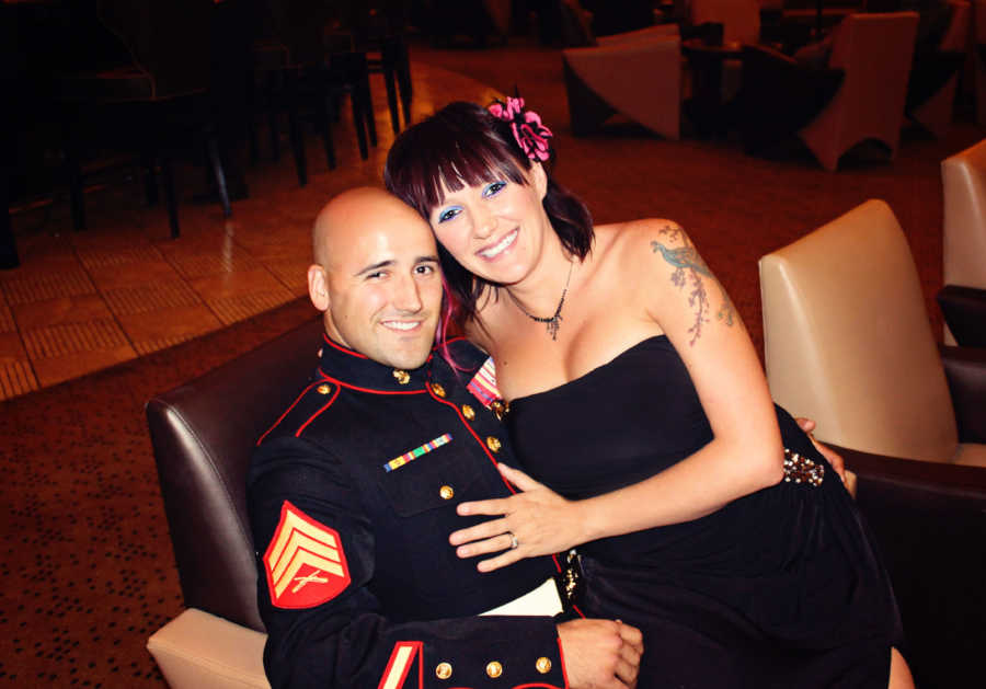 Wife smiles as she sits on marine husband's lap who is sitting in chair