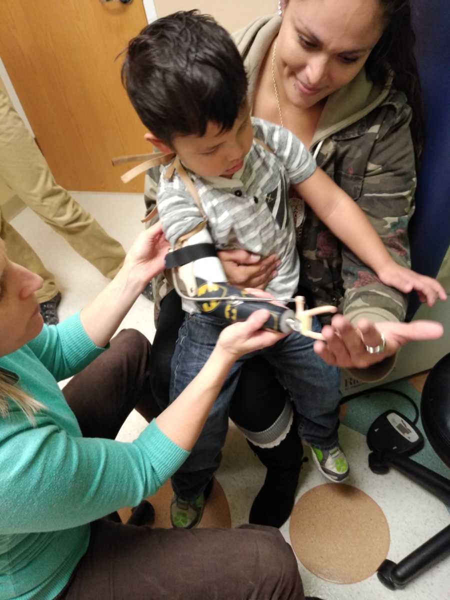 Young boy with prosthetic arm sits on mother's lap in doctor's office touching her hand