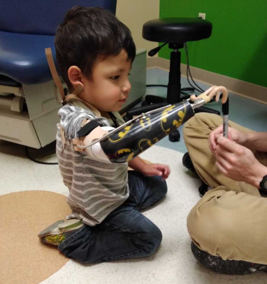 Young boy born without right arm sits on floor of doctor's office with prosthetic arm on 