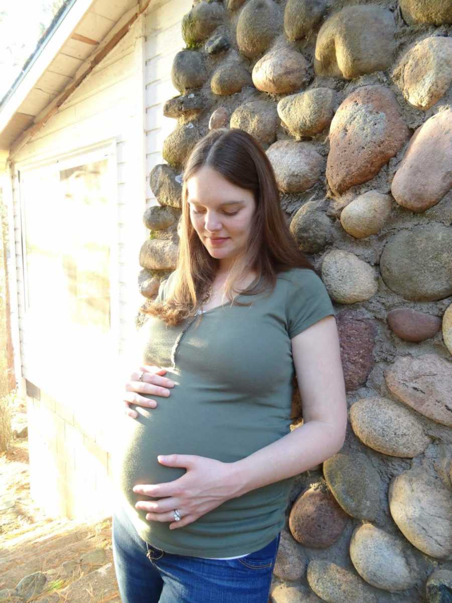 Pregnant woman stands holding her stomach beside stone wall