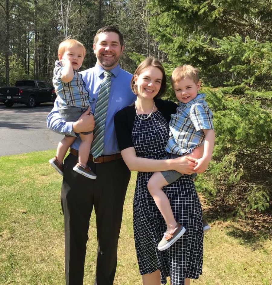 Husband and wife stands outside holding their two sons