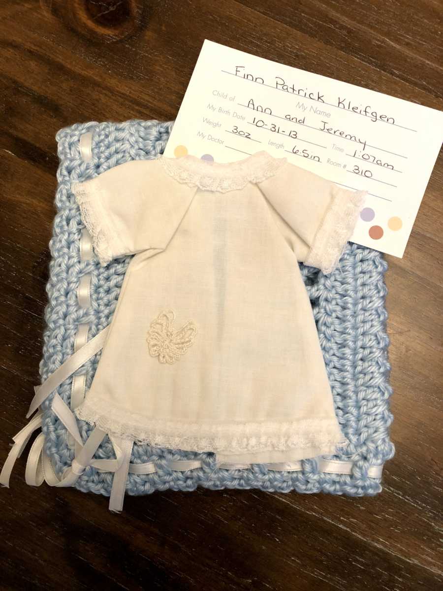 Baby dress laying on blue blanket beside note with information for baby's birth