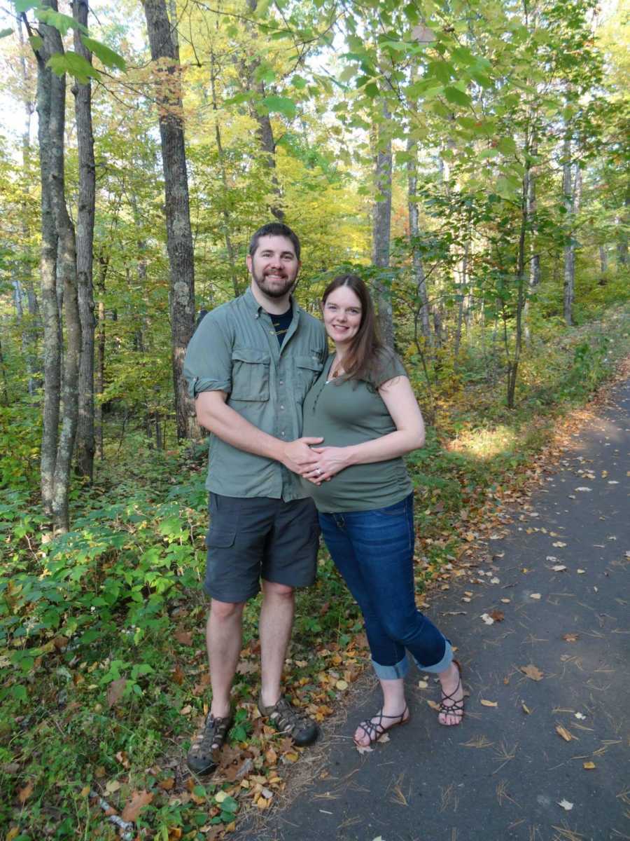 Pregnant woman and husband stand on trail holding her stomach