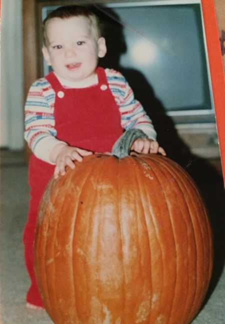 Little boy who will later in life die from smoking a heroin-laced joint standing behind pumpkin