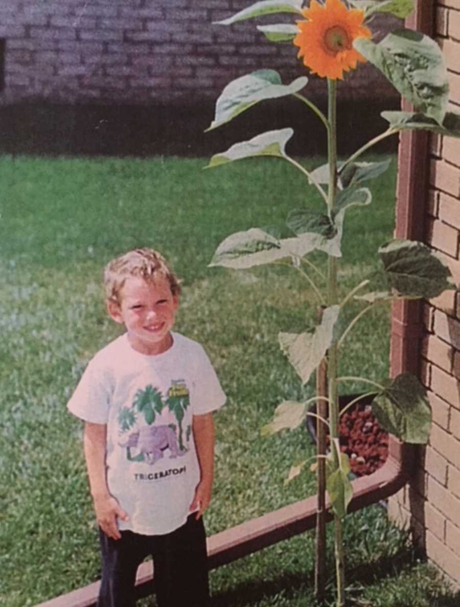 Young boy who will later in life die from smoking a heroin-laced joint standing beside tall sunflower