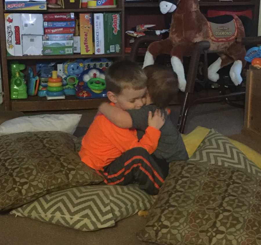 Baby with Febrile Seizures hugs brother as they sit on floor beside pillows