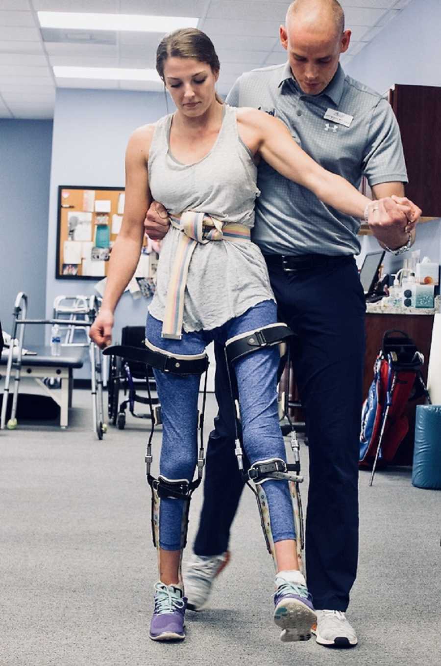 Woman in leg braces trying to walk in physical therapy with boyfriend