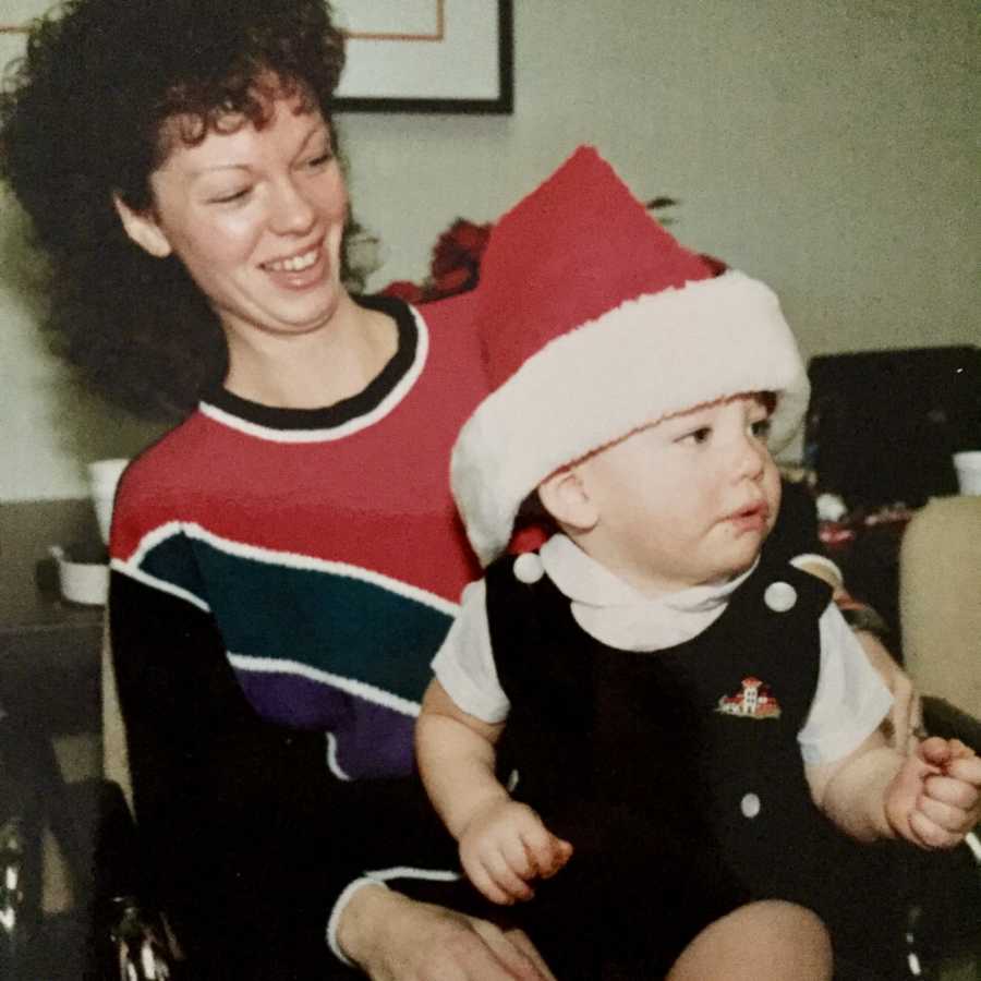 Mother smiles as she baby son with Santa hat on sits in her lap