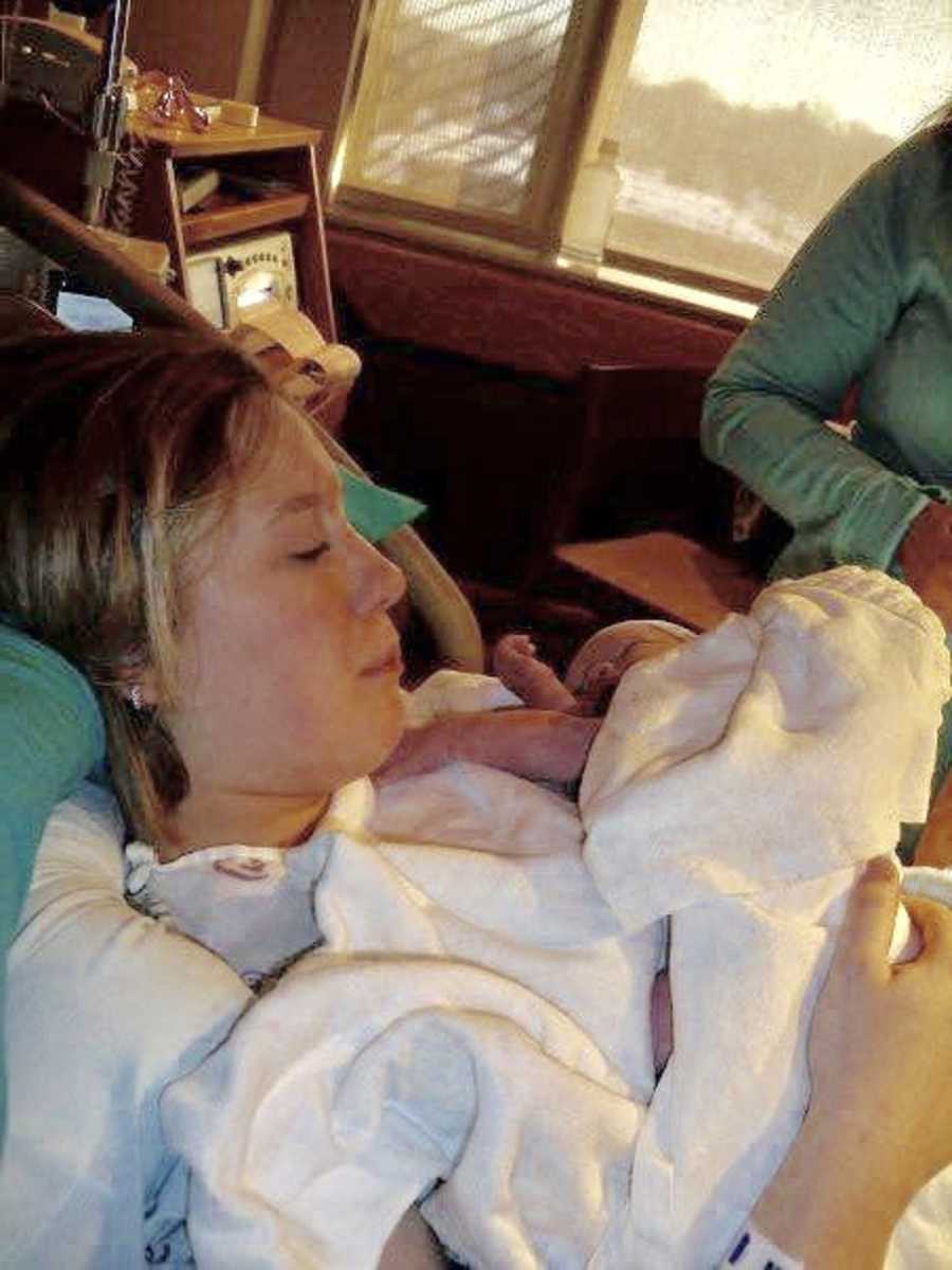 Teen lays in hospital bed looking at her newborn she holds in her arms