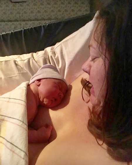 Mother looks down at newborn that is asleep on her bare chest