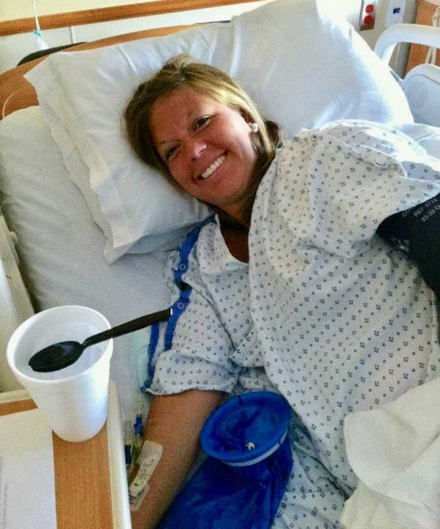Pregnant woman lies on her side in hospital bed smiling beside cup of ice