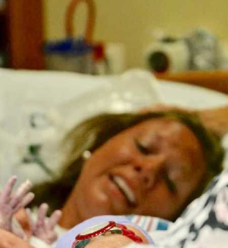 Woman smiles in hospital bed as she looks at newborn 