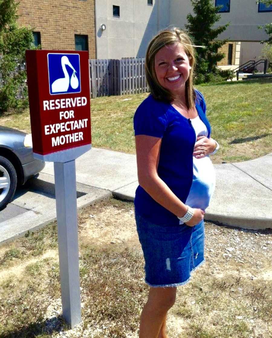 Pregnant woman stands beside sign outside of hospital that says, "Reserved for expectant mother"