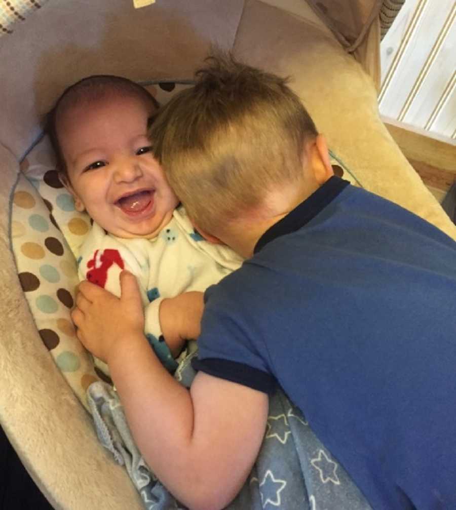 Baby with Febrile Seizures lays smiling while older brother hugs him