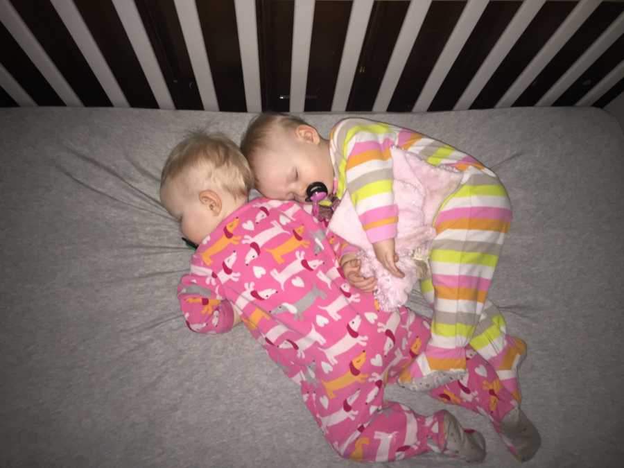 Twins sleep in crib snuggled up together 