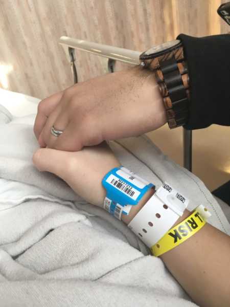 Close up of pregnant woman with hospital bracelet that says, "risk" on it holding husband's hand